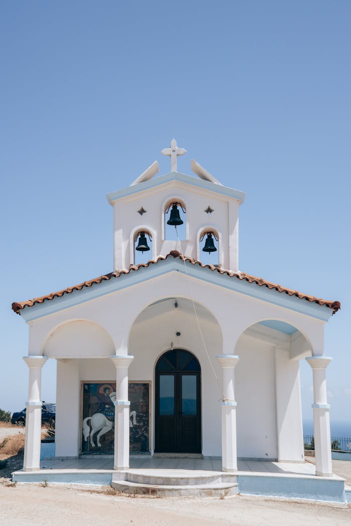 Charming small white chapel in Greece with traditional architecture under a clear blue sky.